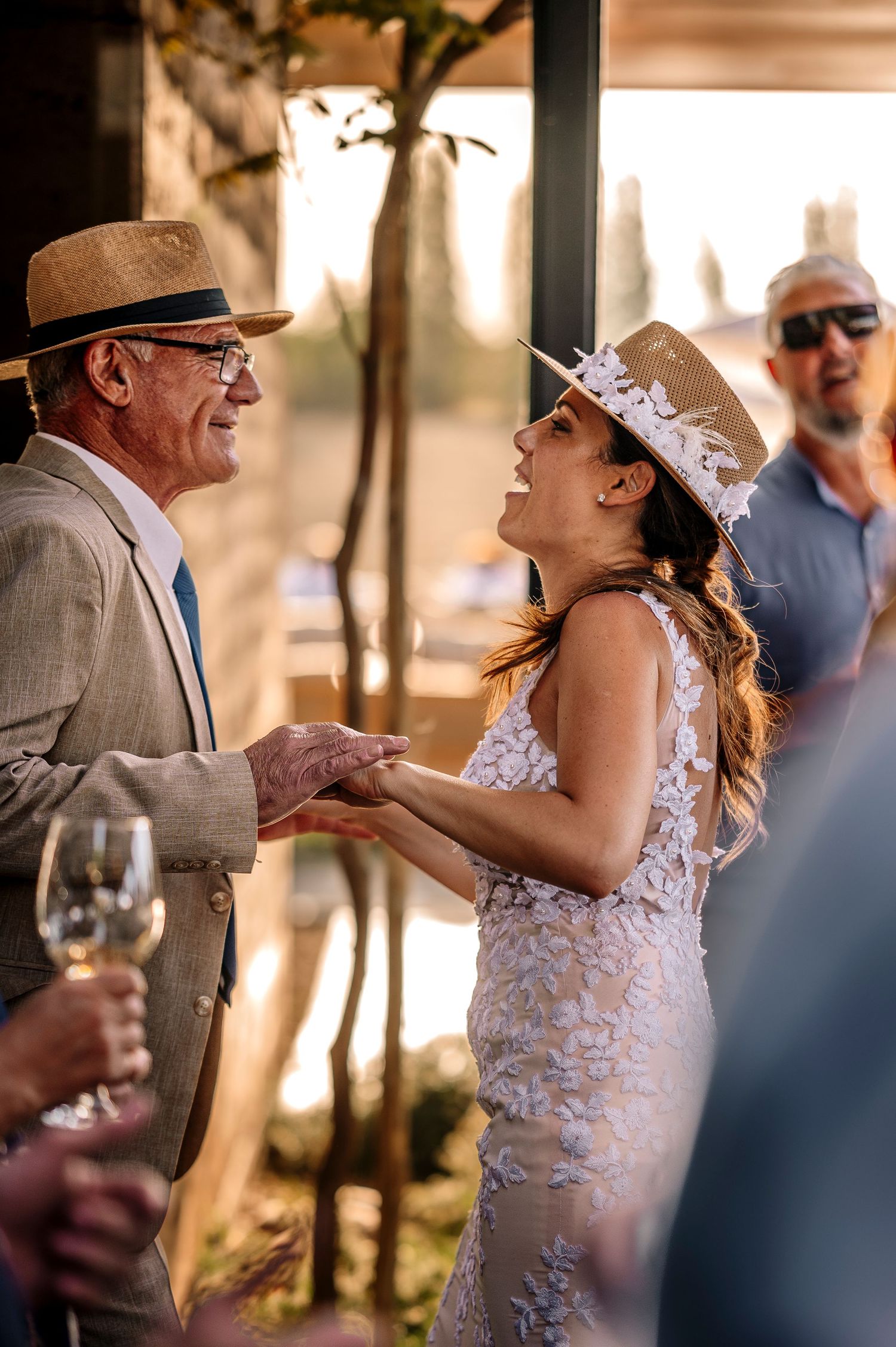 A bride in a lace dress shares an intimate dance with her partner at an outdoor wedding reception during golden hour.
