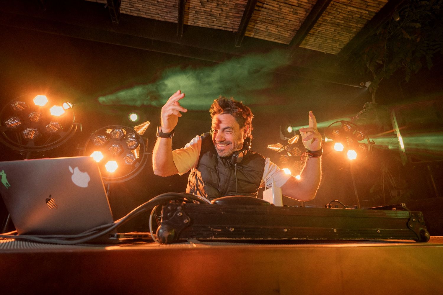 DJ performing at a nightclub with bright orange stage lights and green laser beams in the background.