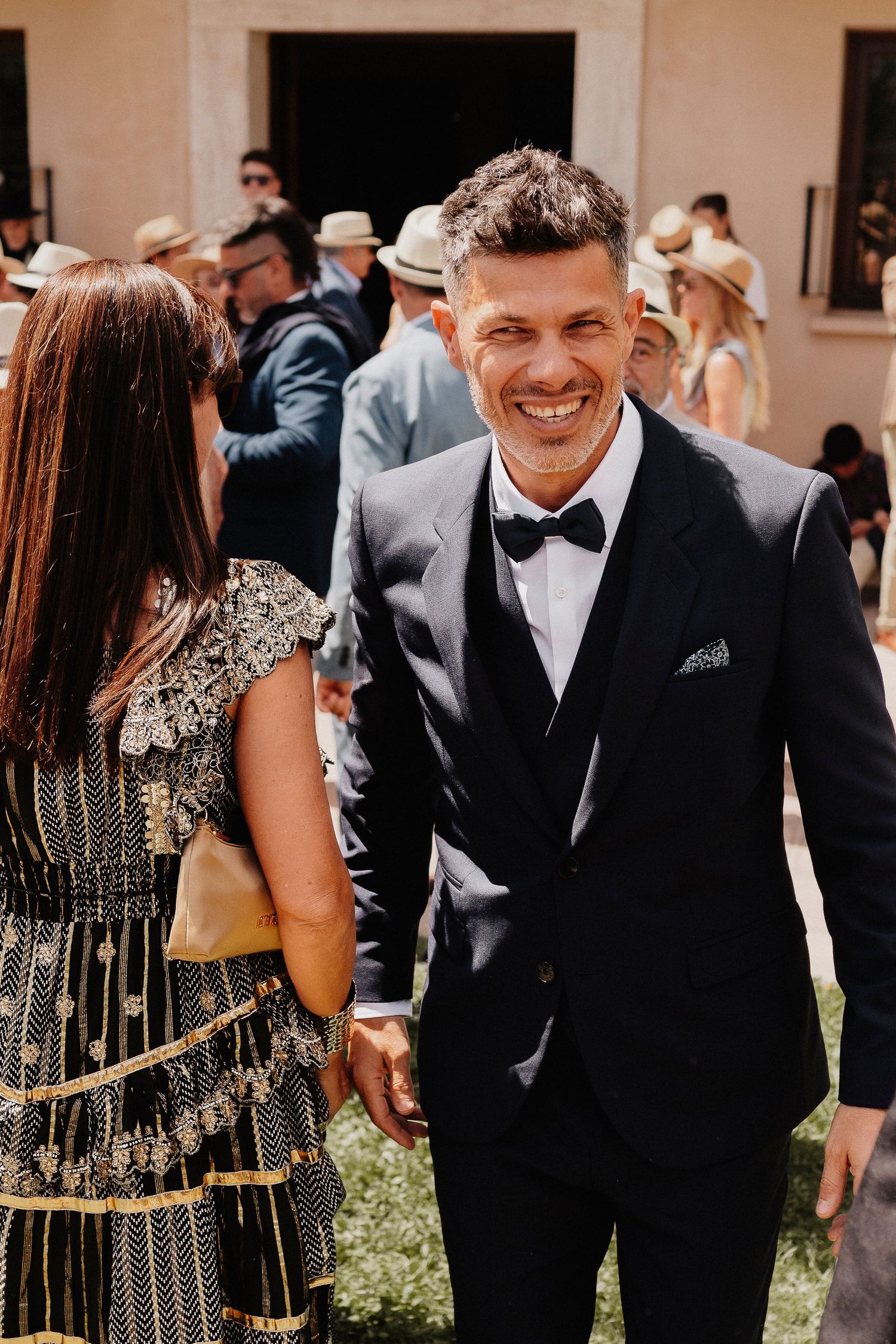 A group of formally dressed guests mingle and interact at an elegant outdoor wedding celebration.