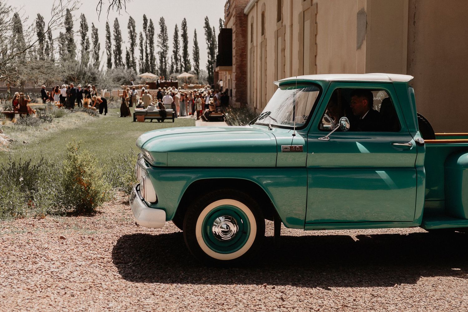 A vintage green car parked in a desert landscape with mountains in the background.