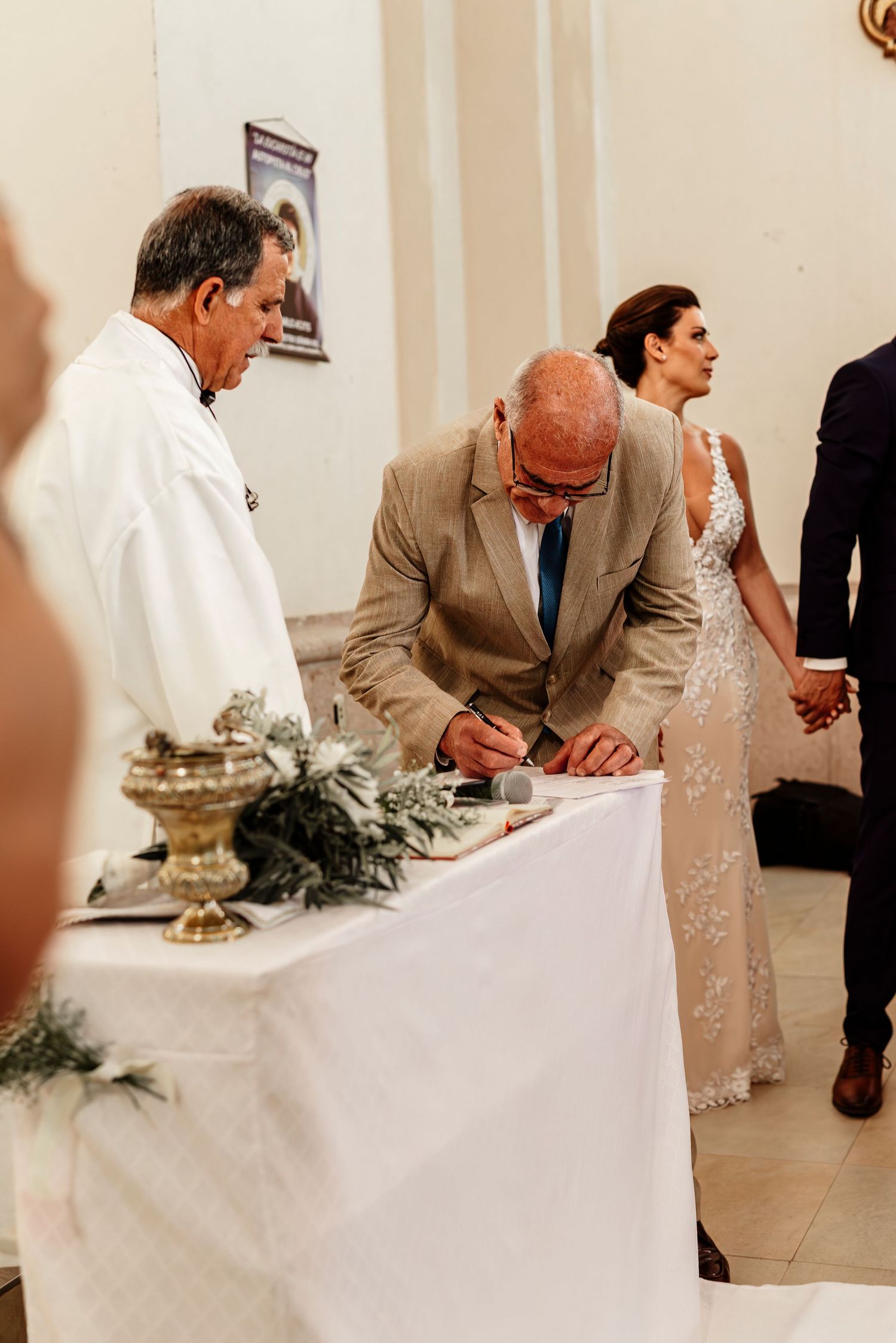 People signing documents at an elegant wedding ceremony with white tablecloth and decorative greenery.