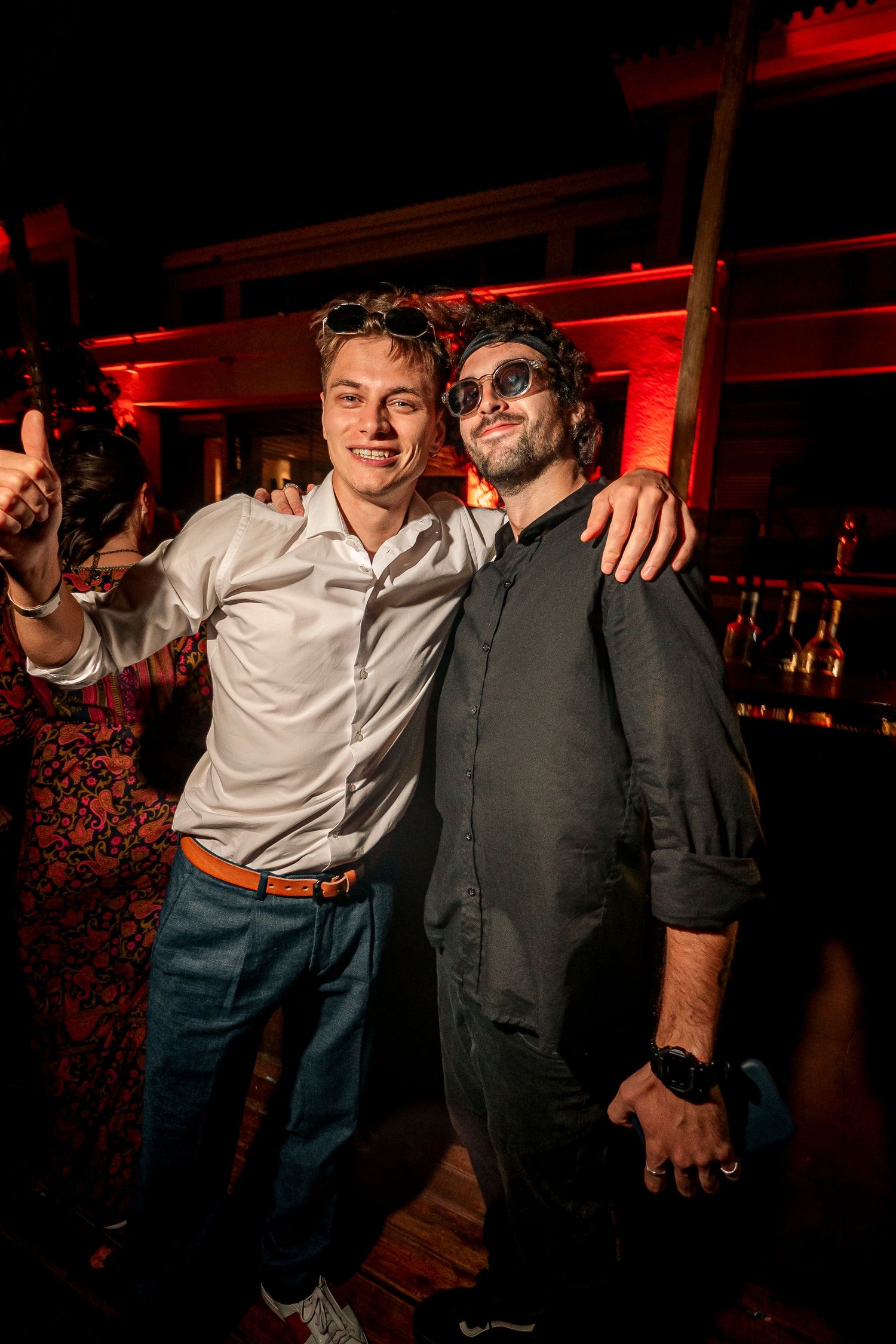 Two friends pose together at a nightclub with red lighting in the background during an evening celebration.
