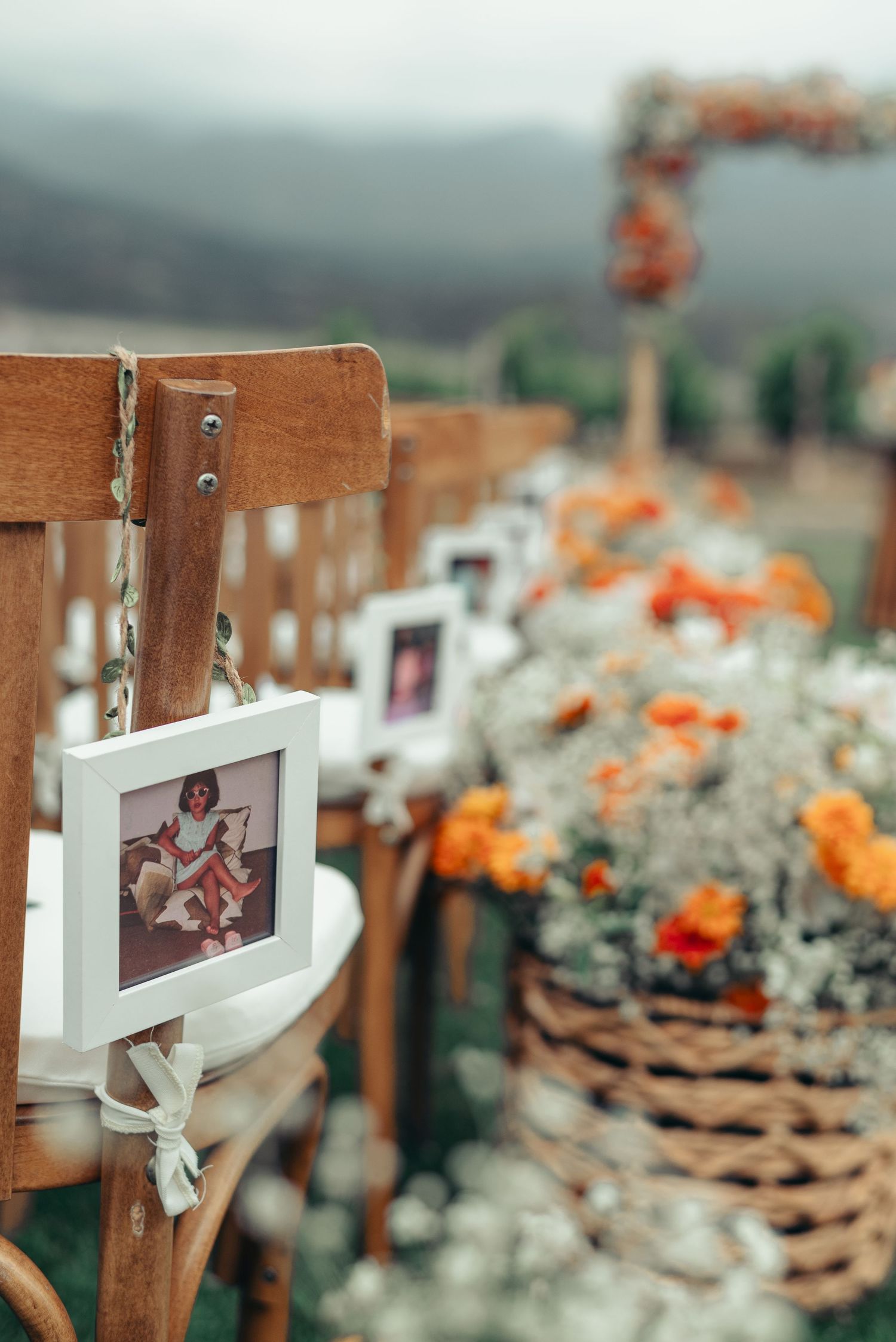 Rustic wooden fence posts decorated with photographs and orange flowers create an intimate outdoor wedding display.