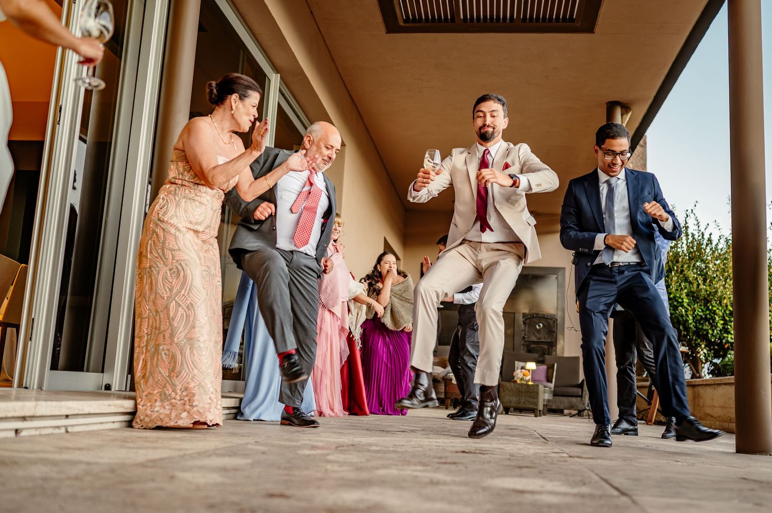 Guests dancing and celebrating joyfully outdoors at a wedding reception on a sunny patio.