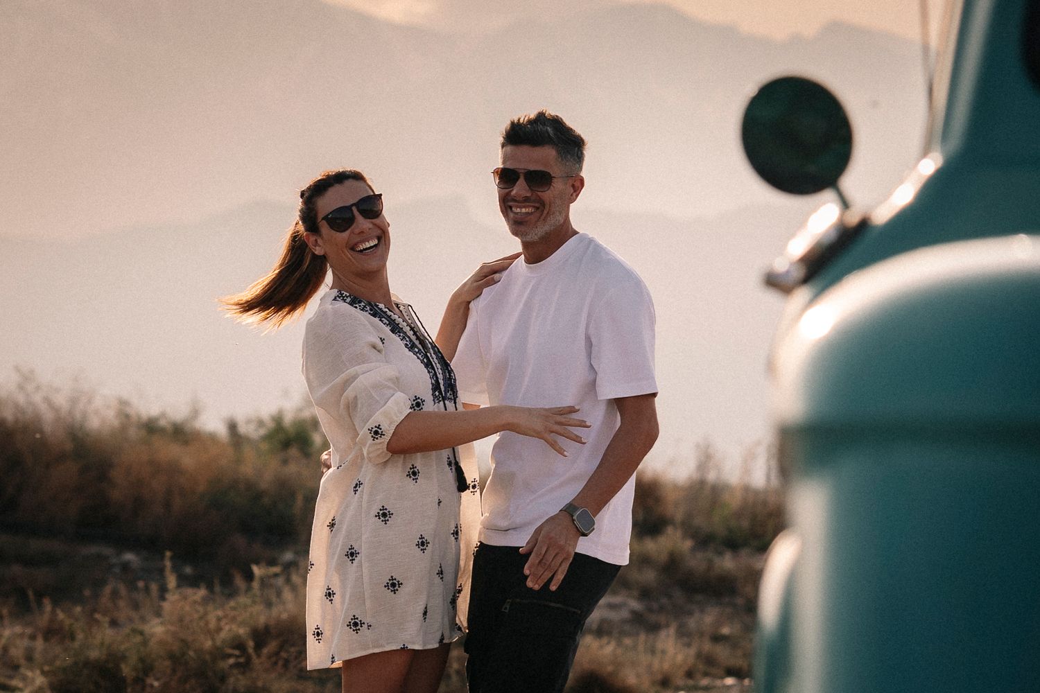 A couple holds hands while walking through a desert landscape at sunset, creating a romantic silhouette.
