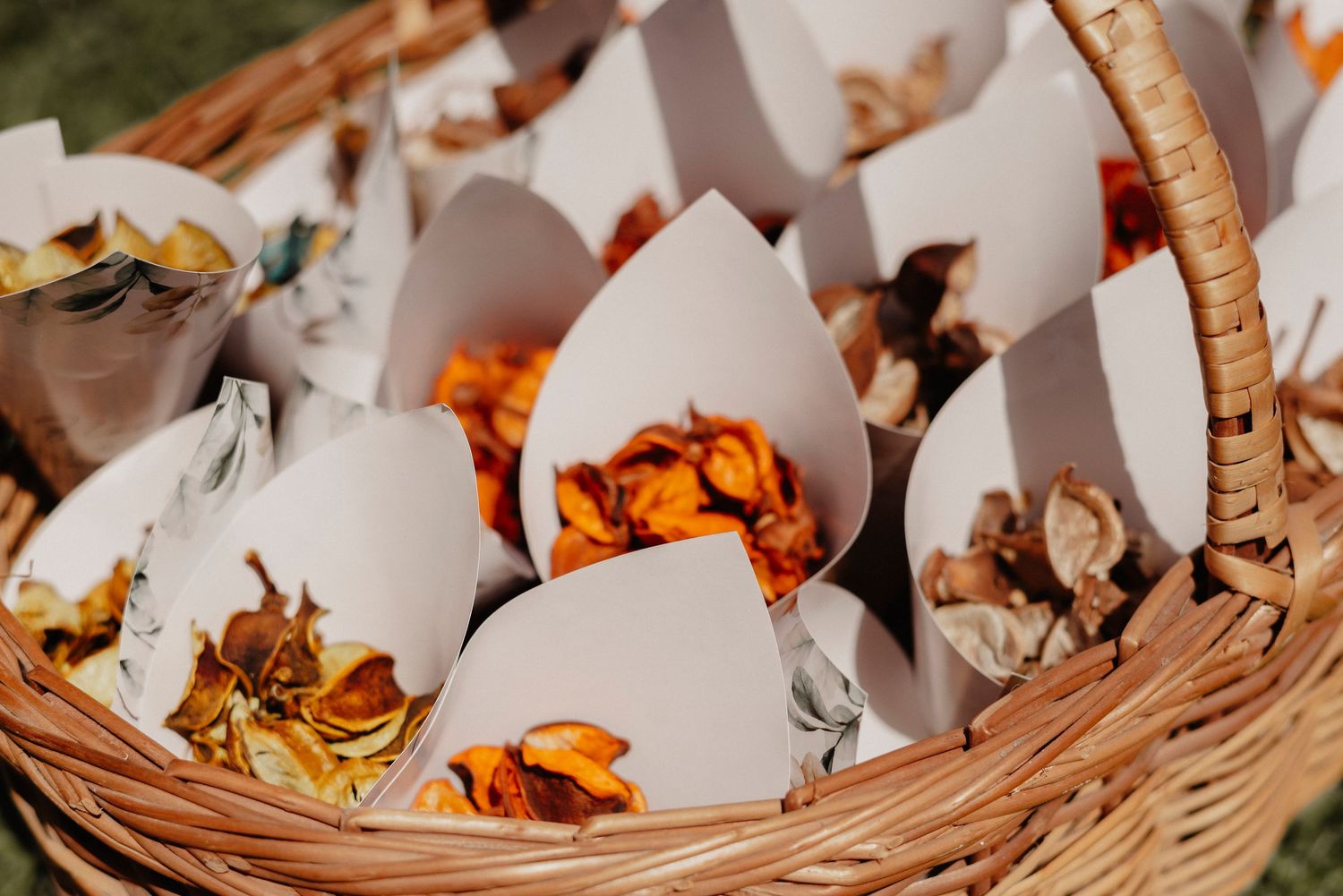 Woven basket filled with small paper cones containing colorful dried flower petals for wedding toss.