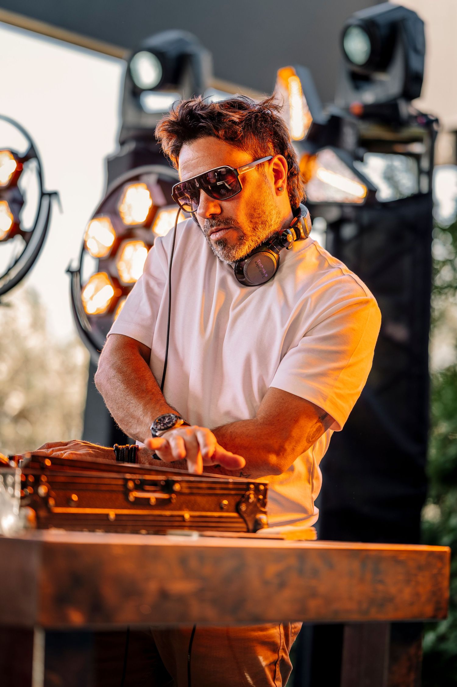 Musician wearing sunglasses plays a wooden dulcimer instrument outdoors during golden hour lighting.