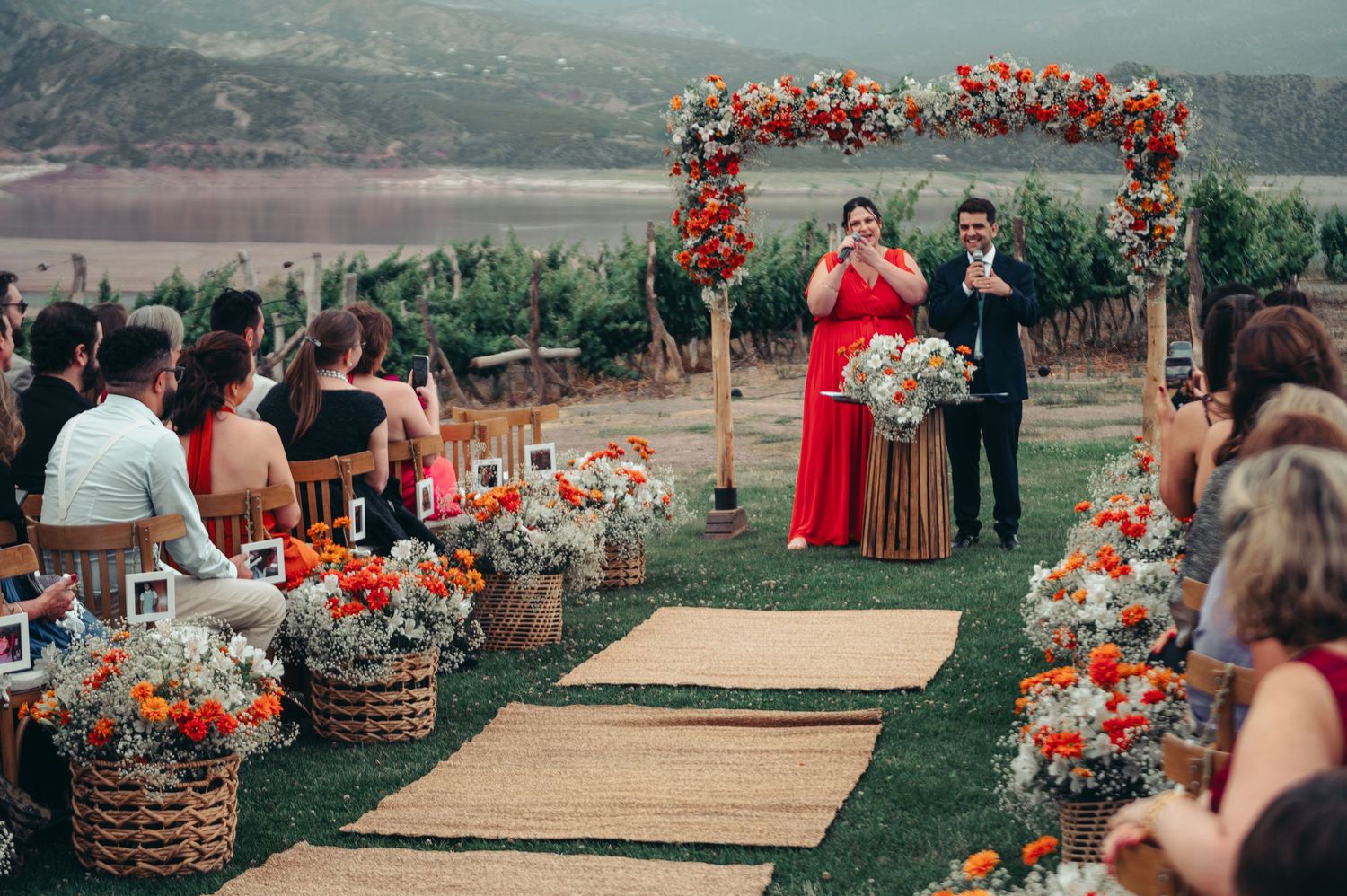 Outdoor wedding ceremony with floral arch and burlap aisle runner overlooking mountain landscape.