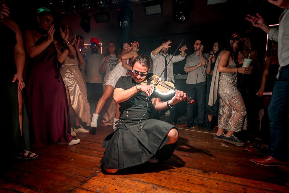 Wedding guests dance and celebrate on a rustic wooden dance floor at an evening reception party.