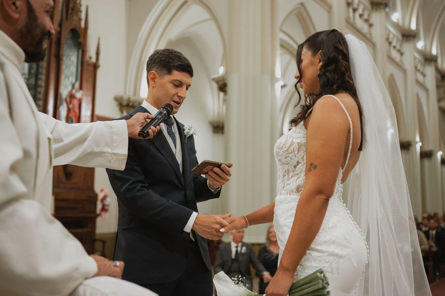 Couple exchanging rings during a church wedding ceremony, officiated by a priest at the altar.