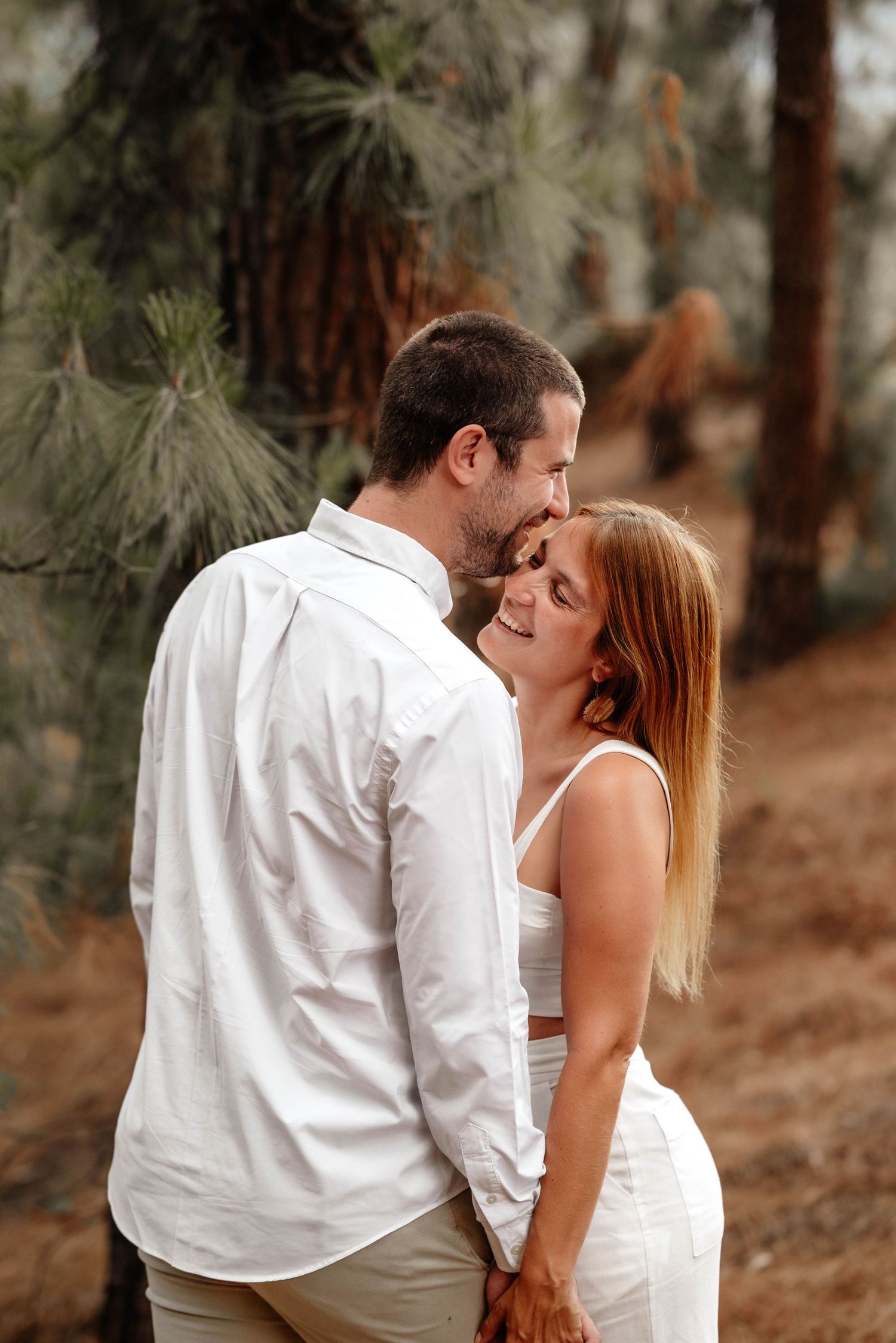 Romantic couple in white outfits share intimate moments in a forest setting during a photo session. pre boda in mendoza