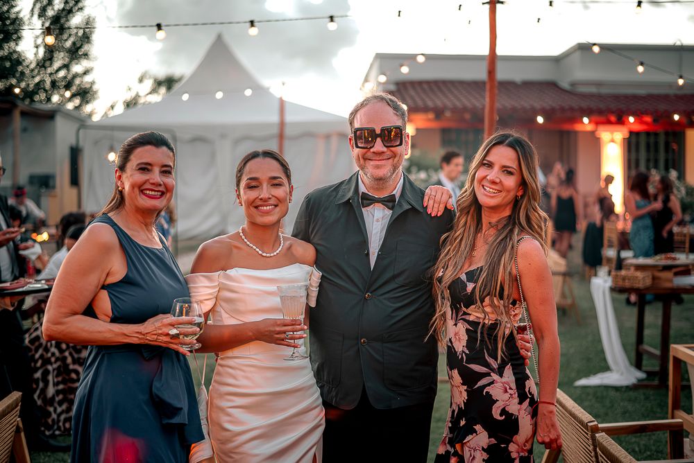 A group of friends pose together at an outdoor evening event with string lights and a tent in the background.