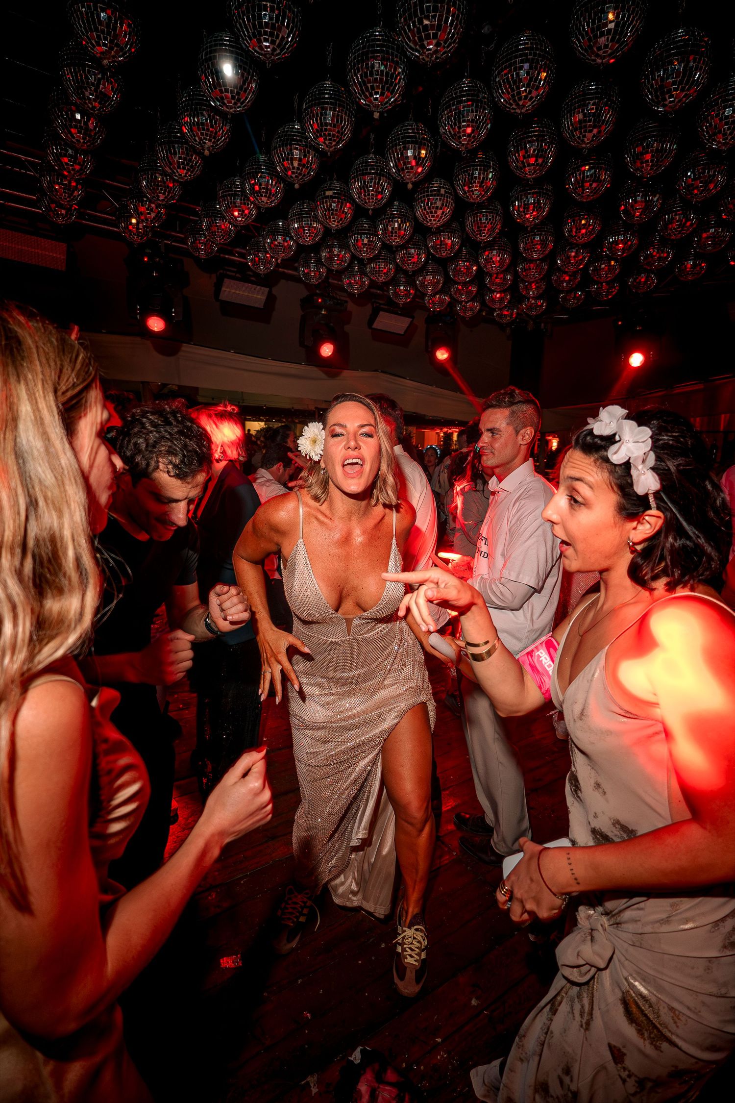 People dancing and socializing at a dimly lit nightclub with red lighting and a festive atmosphere.