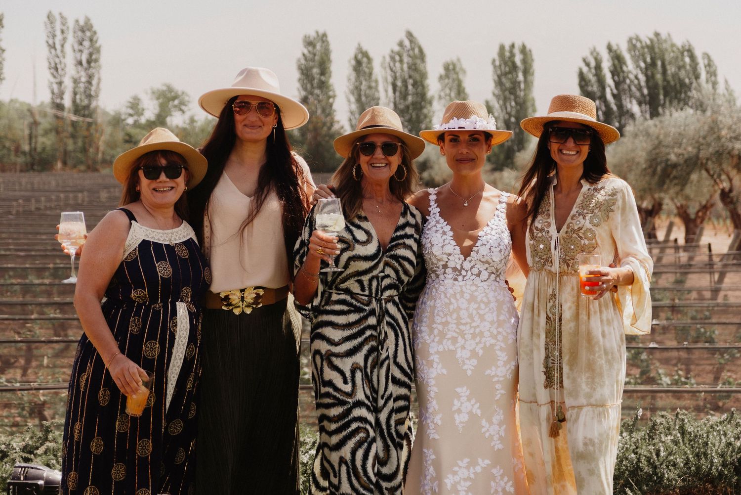Group of friends wearing summer dresses and hats pose together in a garden setting.