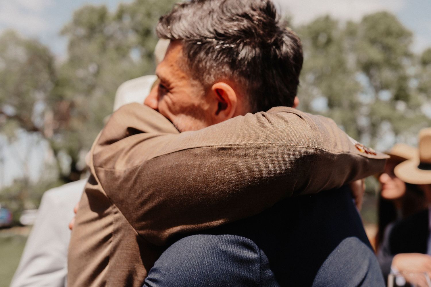 A couple embraces during a sunny outdoor photo session wearing brown and beige tones.