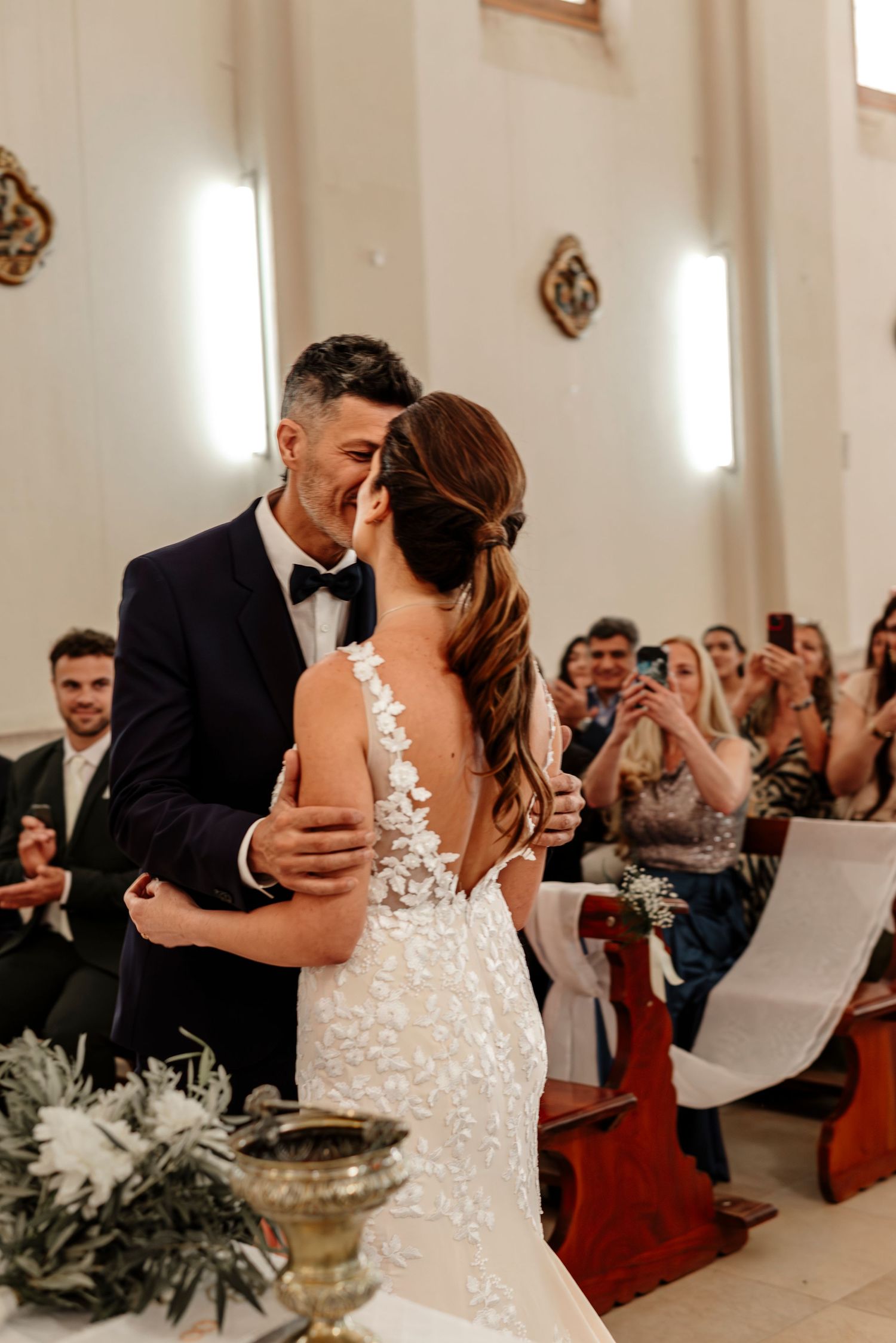 Newlyweds share their first dance in an elegant white church venue surrounded by wedding guests.