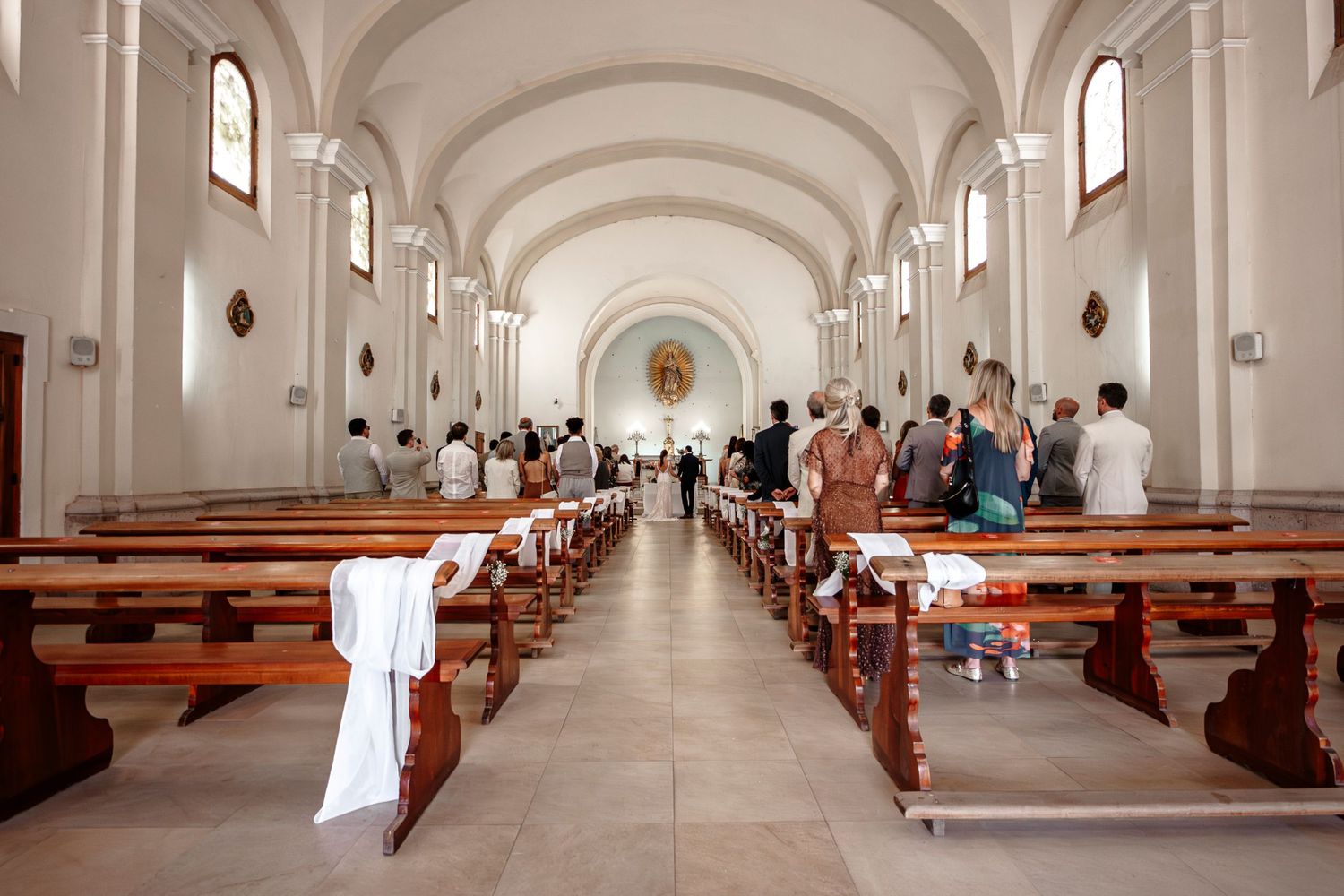 Interior view of a white church sanctuary with wooden pews and arched windows creating a symmetrical perspective.