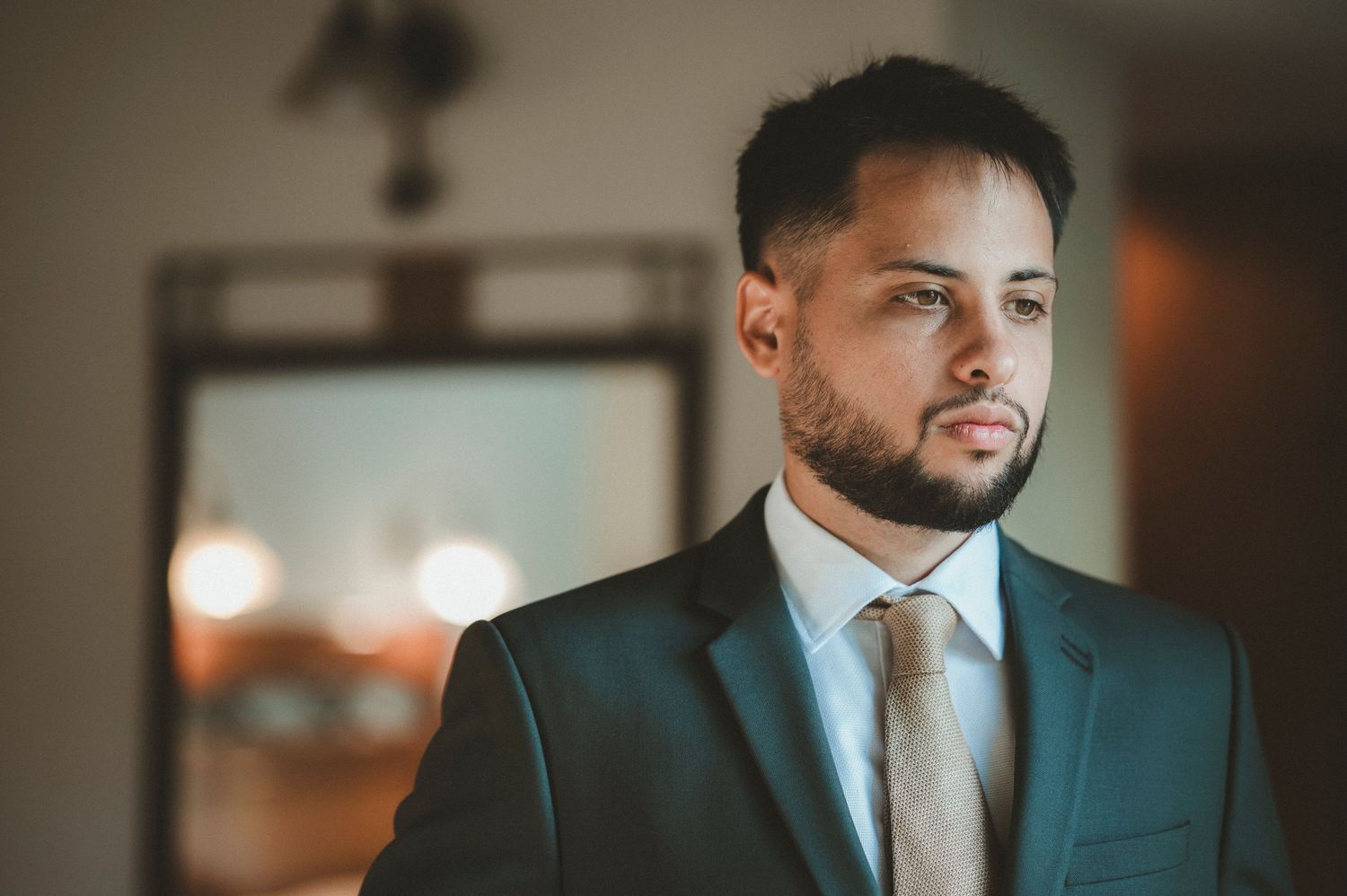 A person in a dark suit and tie smiles while seated in an elegant indoor setting with warm lighting.