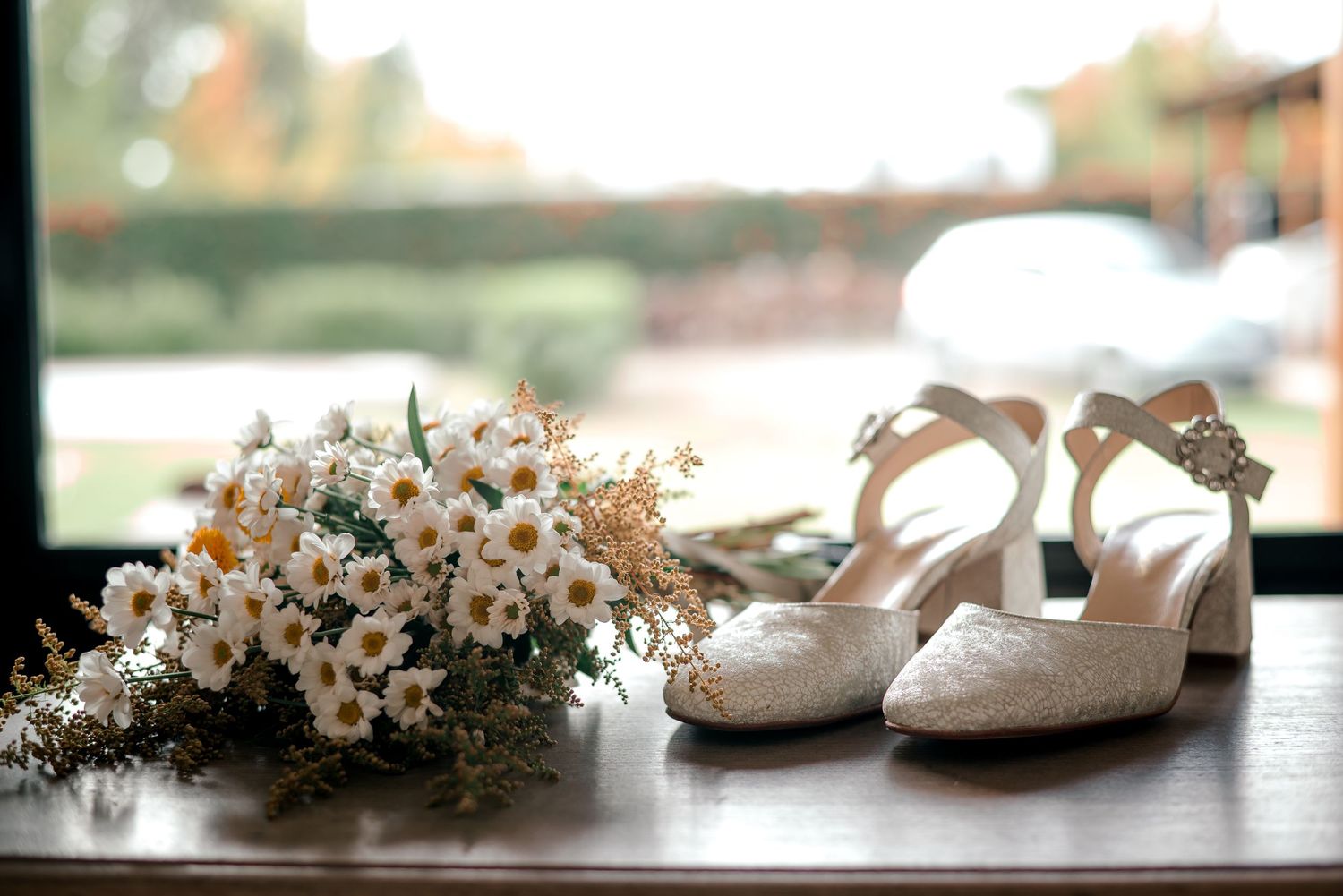 White lace bridal shoes and delicate baby's breath bouquet arranged on windowsill in soft natural lighting.