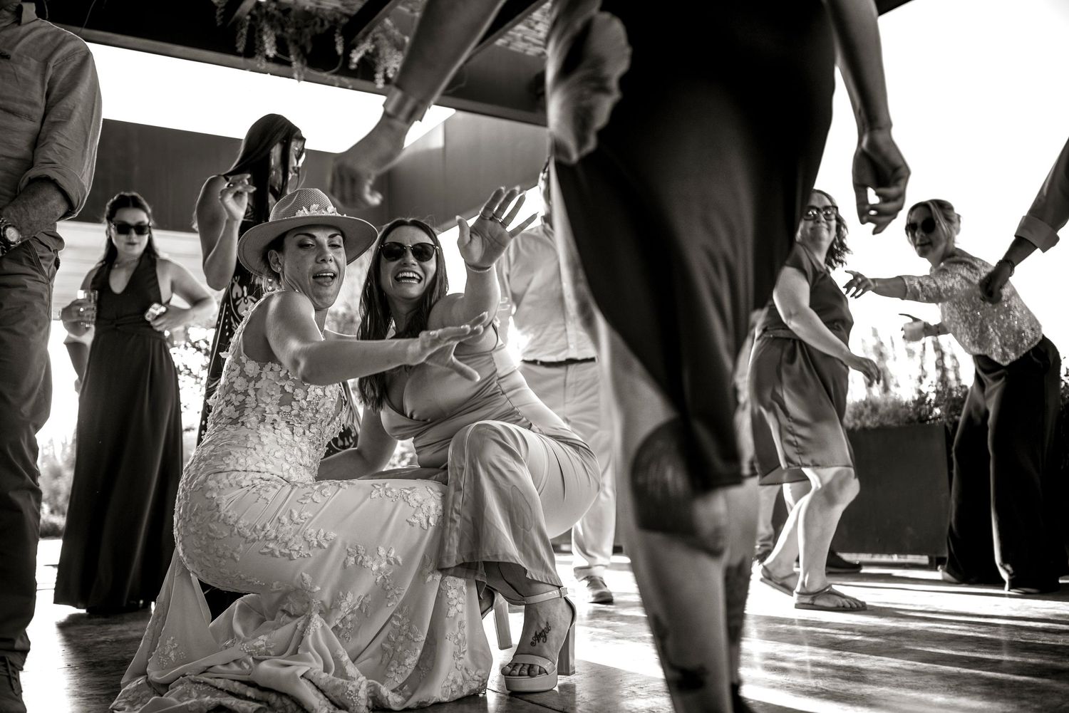 Black and white photo of people dancing and celebrating at a lively wedding reception on a dance floor.