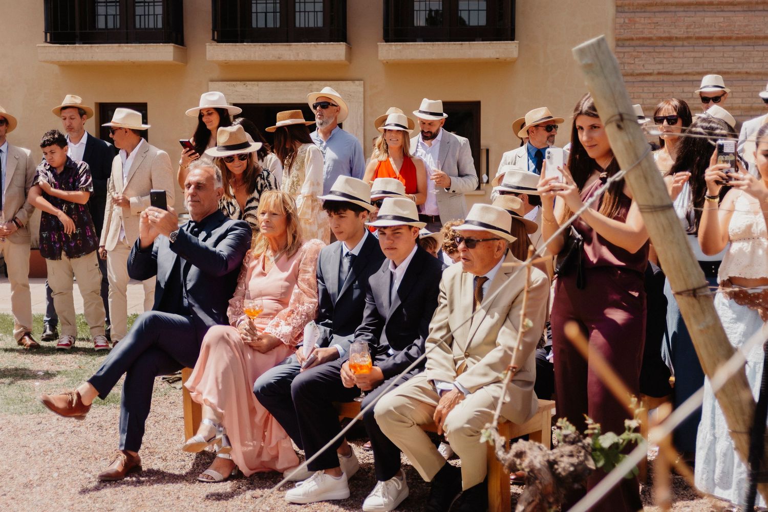 Wedding guests in formal attire dance together in a line formation during an outdoor celebration.