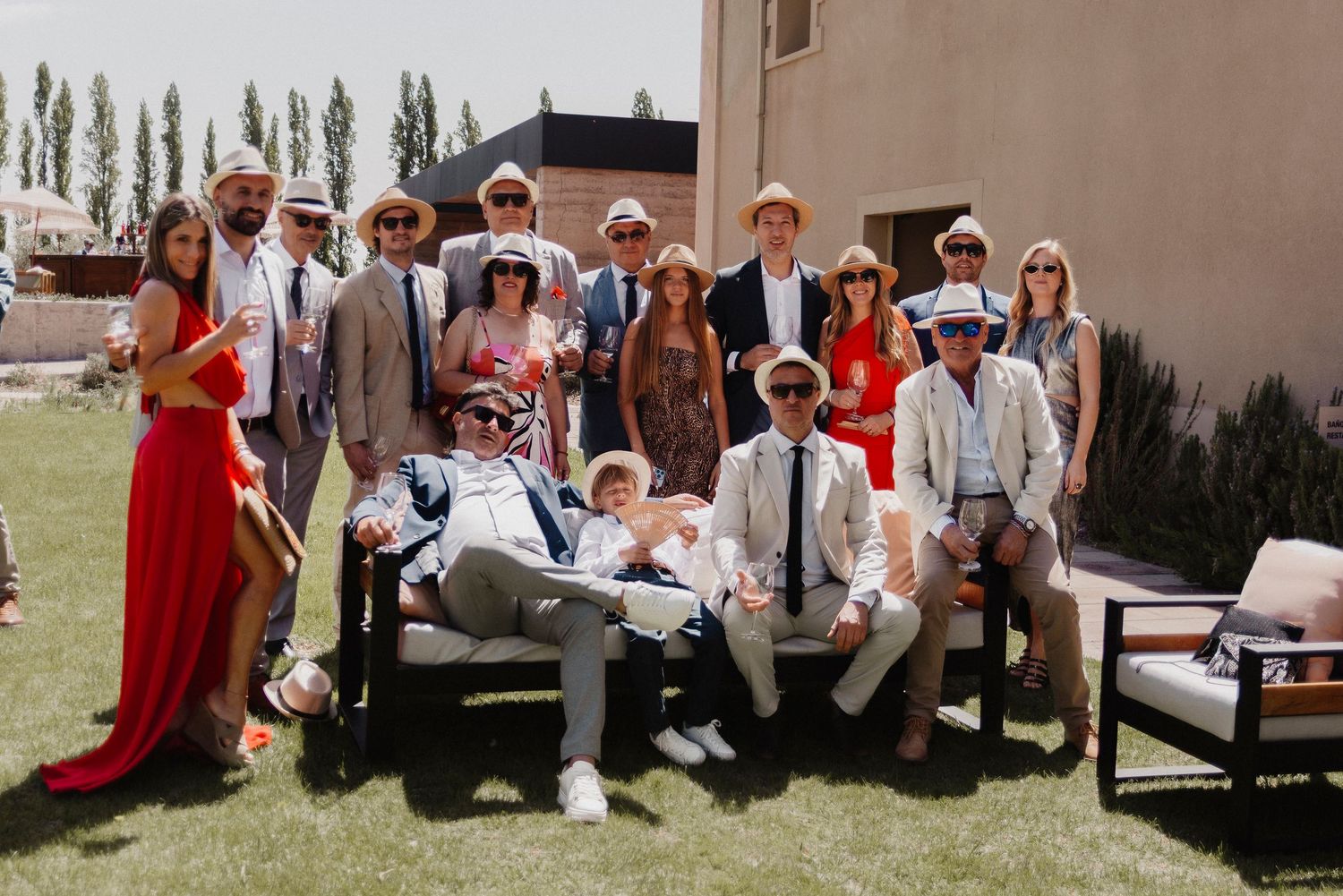 Wedding party members sit together on outdoor benches and steps during a casual moment at a celebration.
