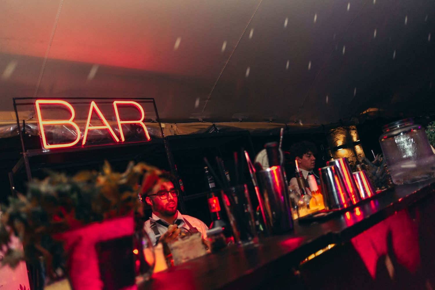 A dimly lit nightclub interior with red neon lighting and bar seating visible in the background.