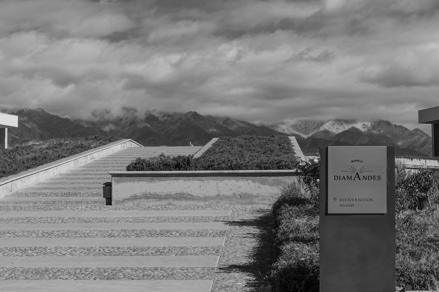 Black and white photo of Toamasina winery entrance with mountain backdrop and dramatic cloudy sky.