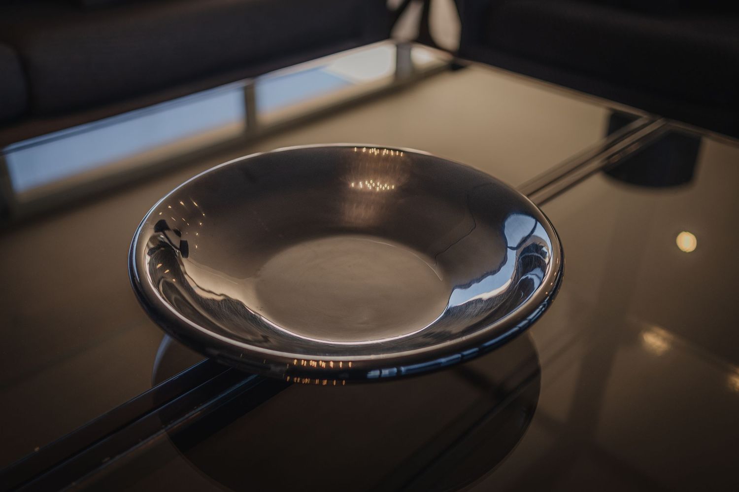 A shiny silver bowl resting on a dark reflective table surface in dramatic moody lighting.