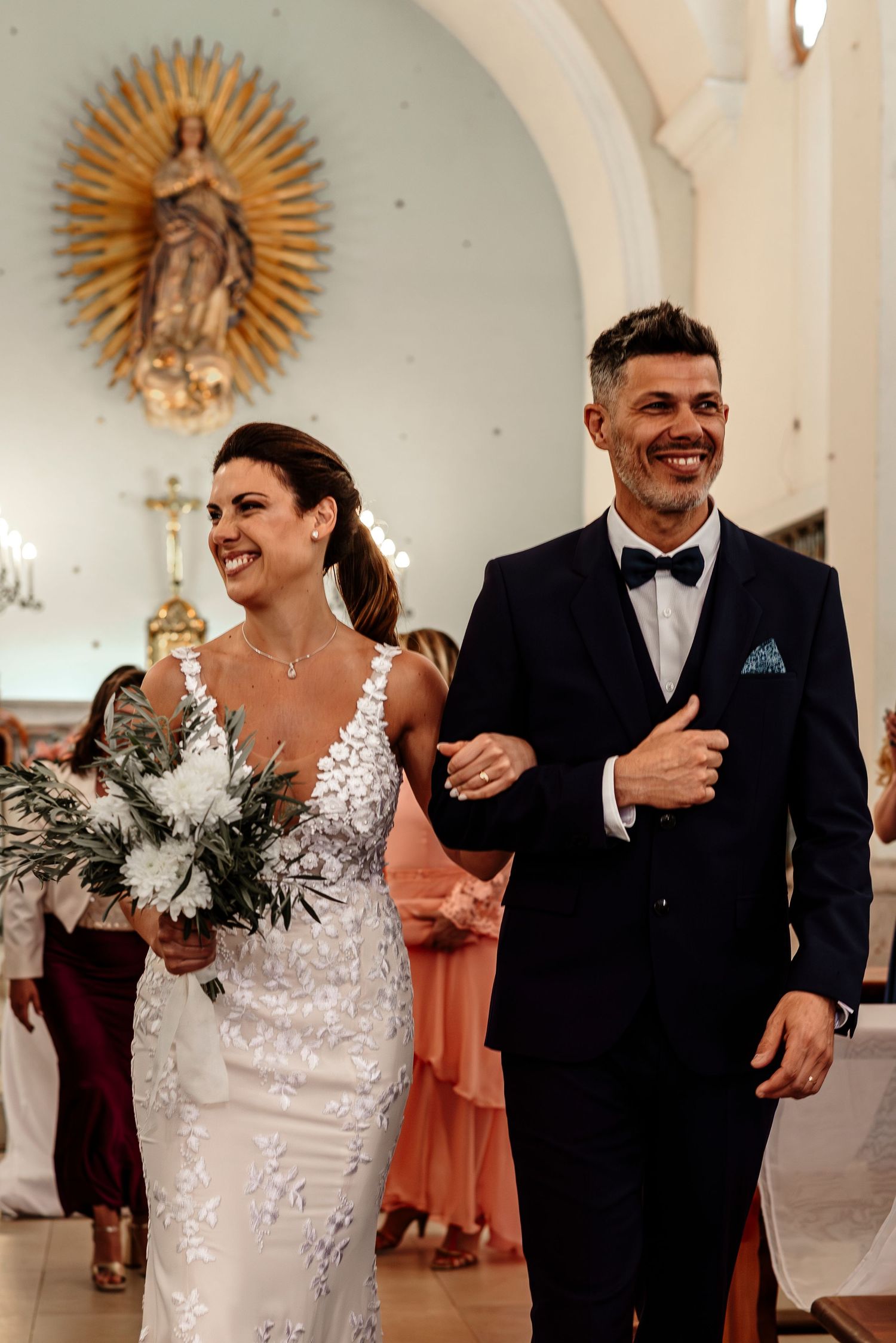 A couple shares joyful laughter while walking together in a church with ornate sunburst decorations on the wall.