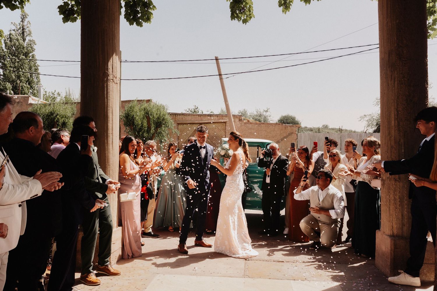 A wedding ceremony takes place in an outdoor venue with guests seated in rows under a covered area.