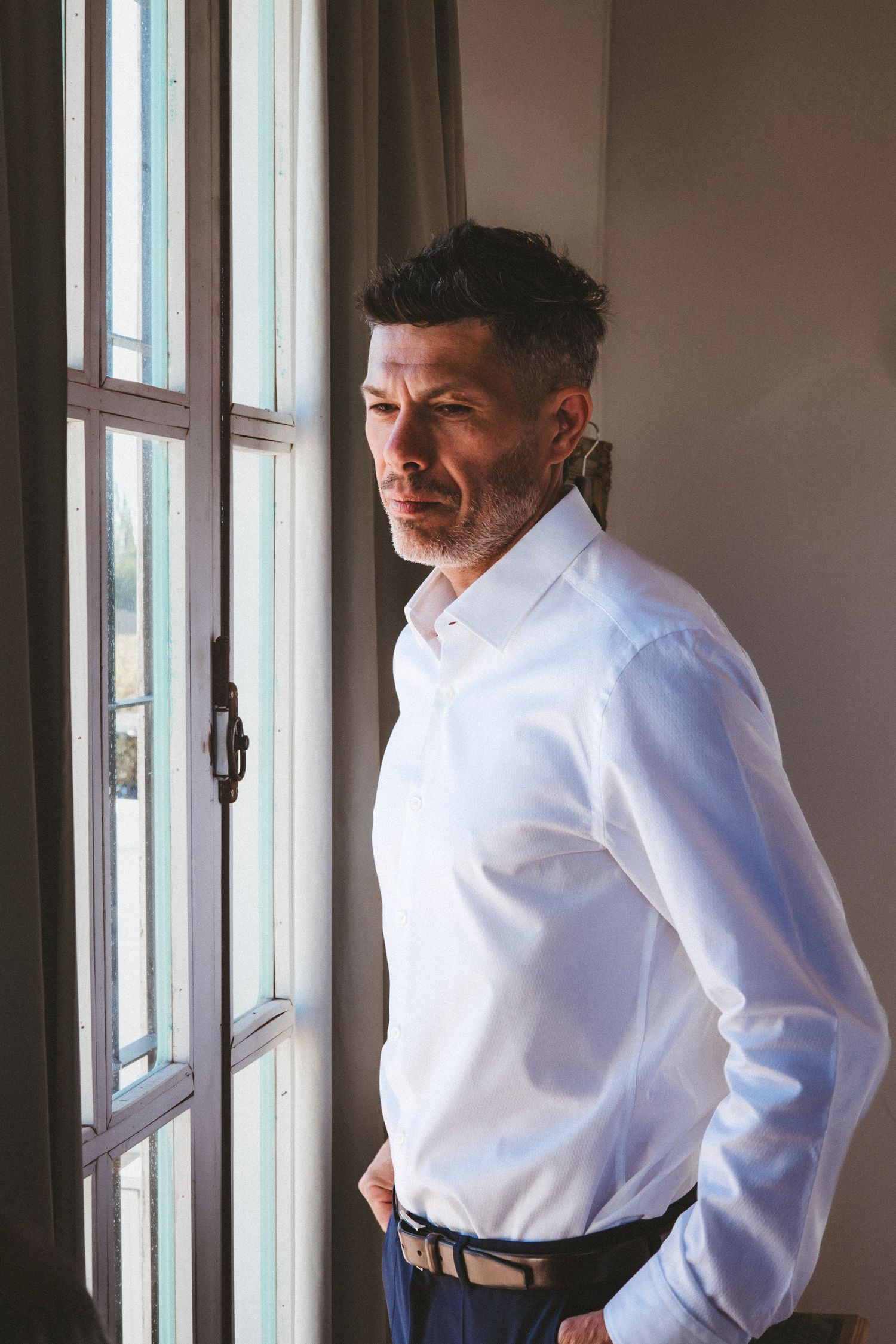 A person wearing a crisp white dress shirt stands near windows in an indoor setting.