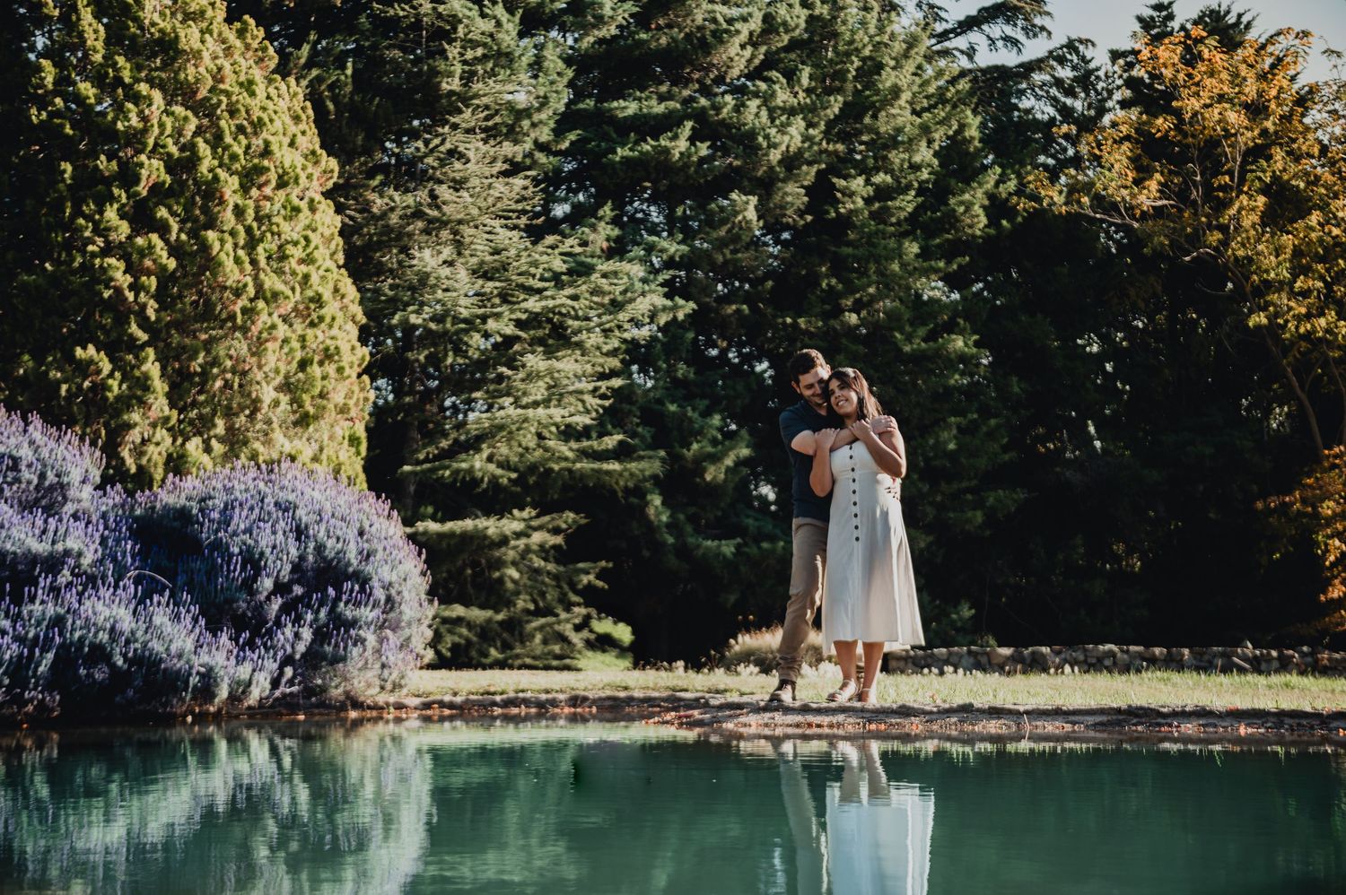 Couple enjoying romantic moments in a lush garden setting during a sunny summer day beside a serene pond.