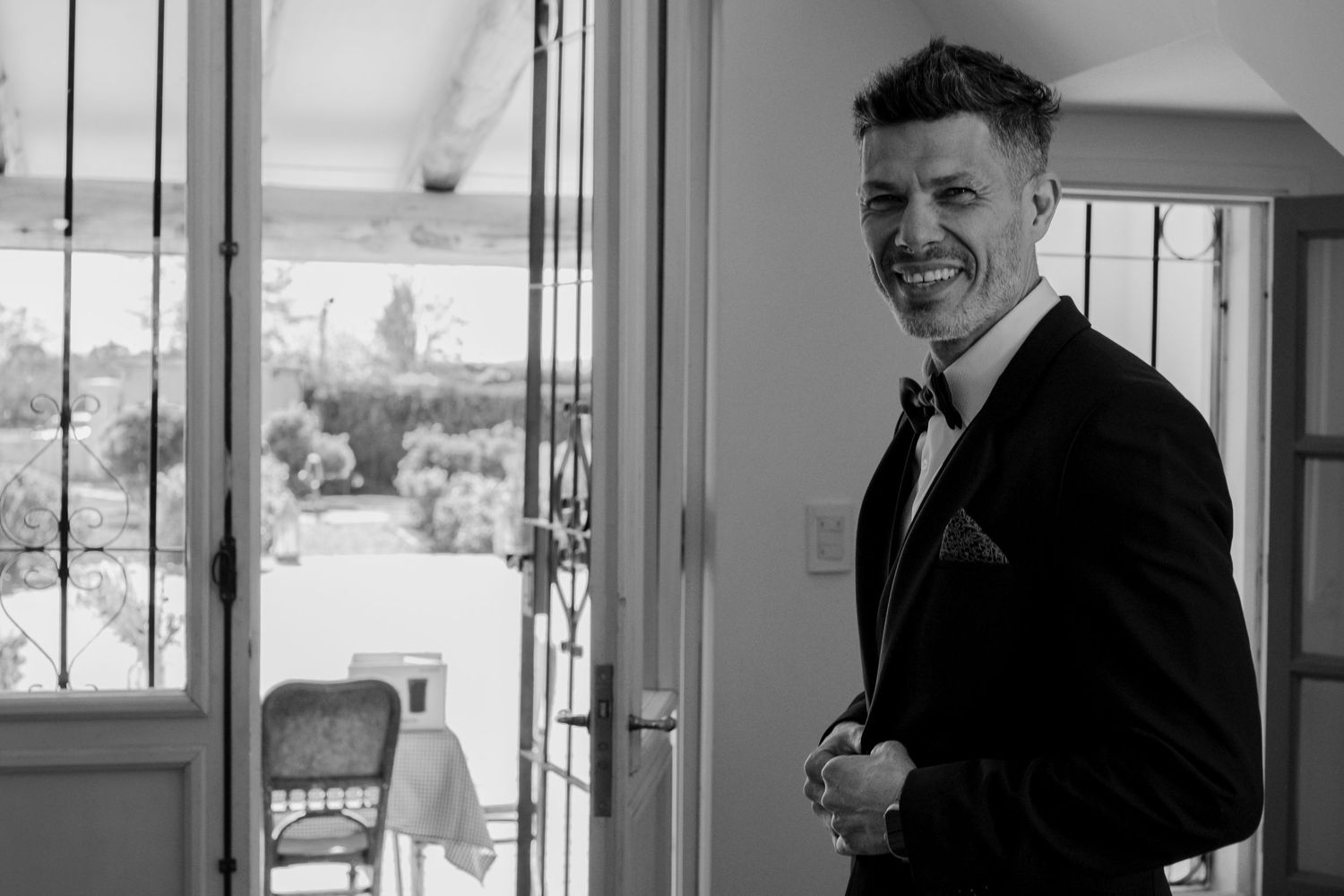 A black and white photo shows a person in a suit smiling and holding a cup while standing in an office hallway.