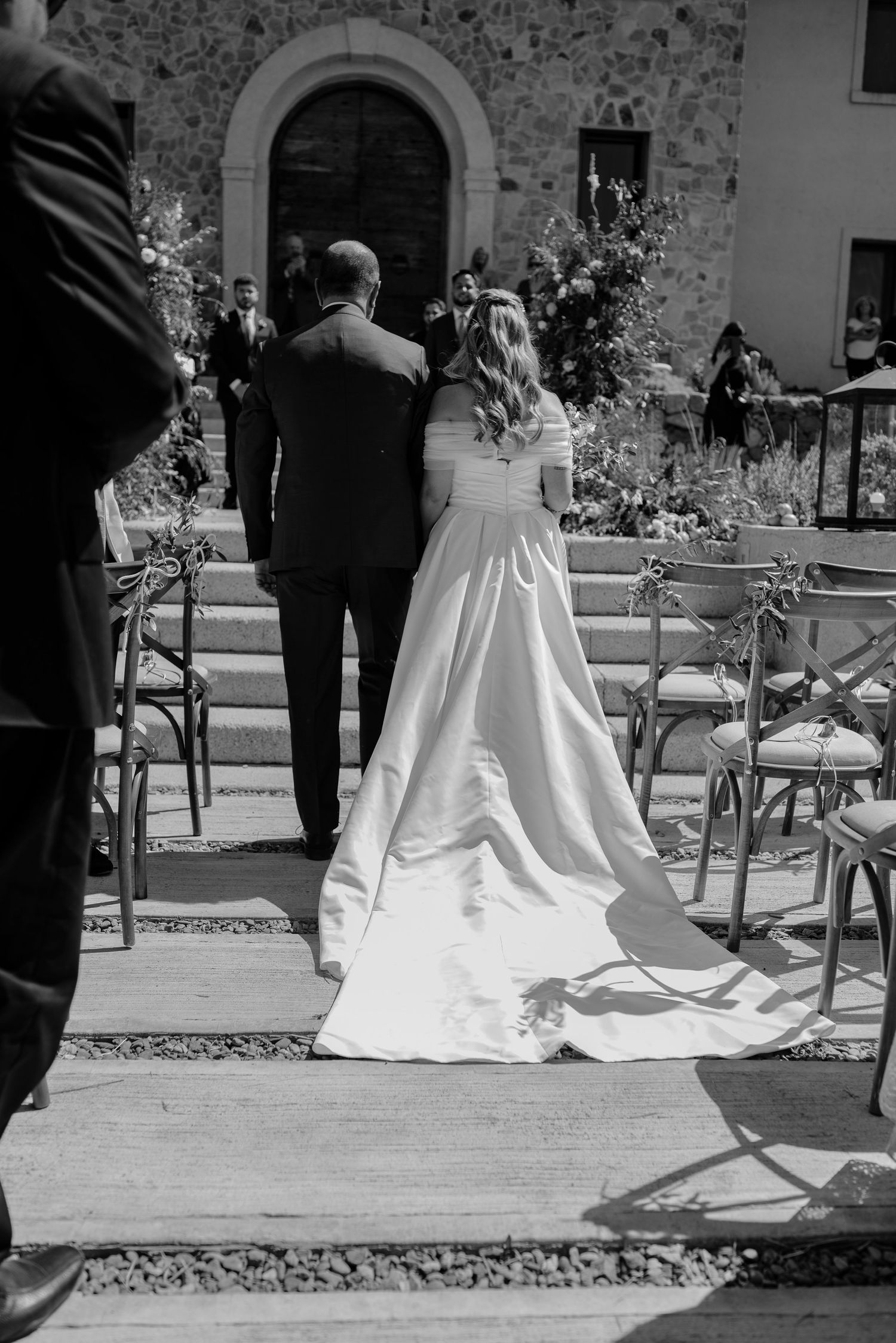 Black and white wedding photo sequence showing a bride's flowing white dress train trailing behind on stone pavement.