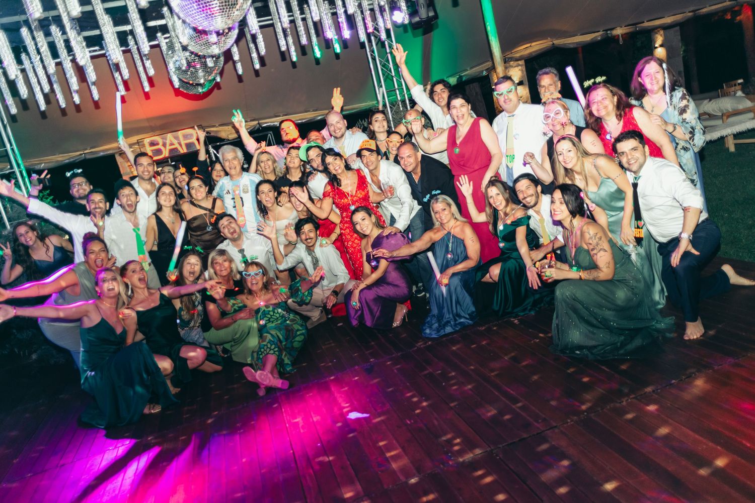 Crowd of party-goers dancing and celebrating on a nightclub dance floor with vibrant purple lighting effects.