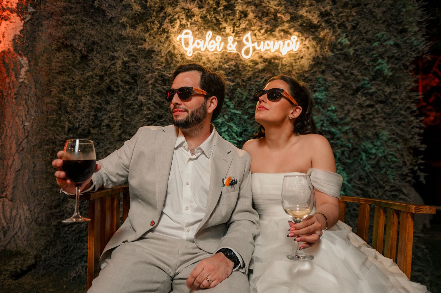 A couple in formal attire enjoying drinks at an outdoor garden venue with string lights overhead. fotografos de boda en mendoza