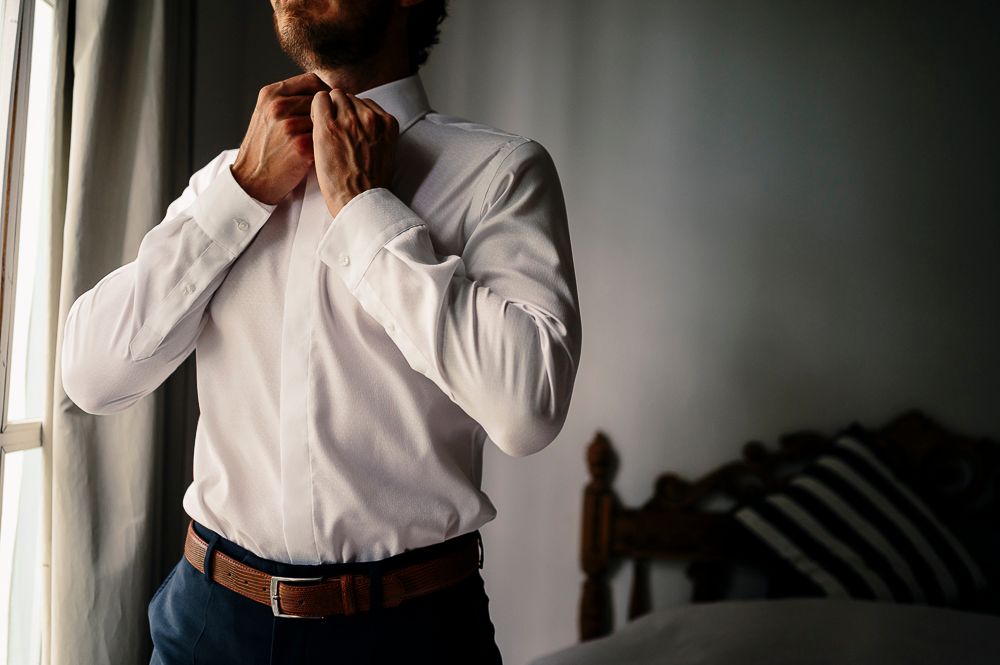 Person in white shirt and dark pants adjusting clothing by a window in dramatic lighting. wedding in mendoza