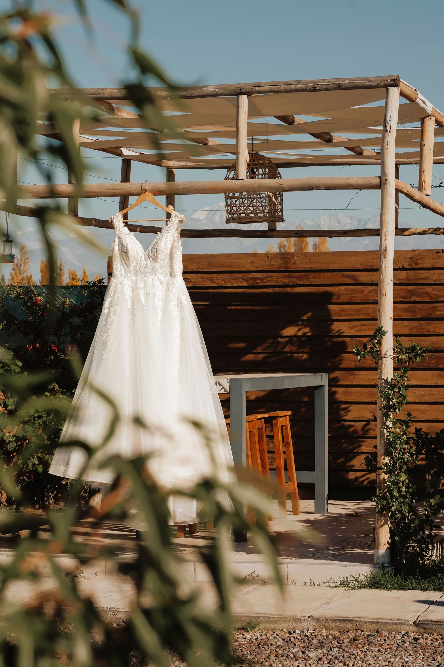 White wedding dress hangs on wooden pergola structure in outdoor desert setting with soft natural lighting.