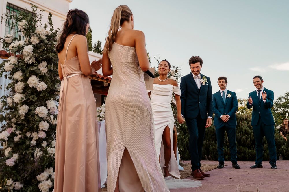 Wedding party stands at outdoor ceremony with bridesmaids in blush gowns and groomsmen in navy suits by floral arch. wedding in mendoza