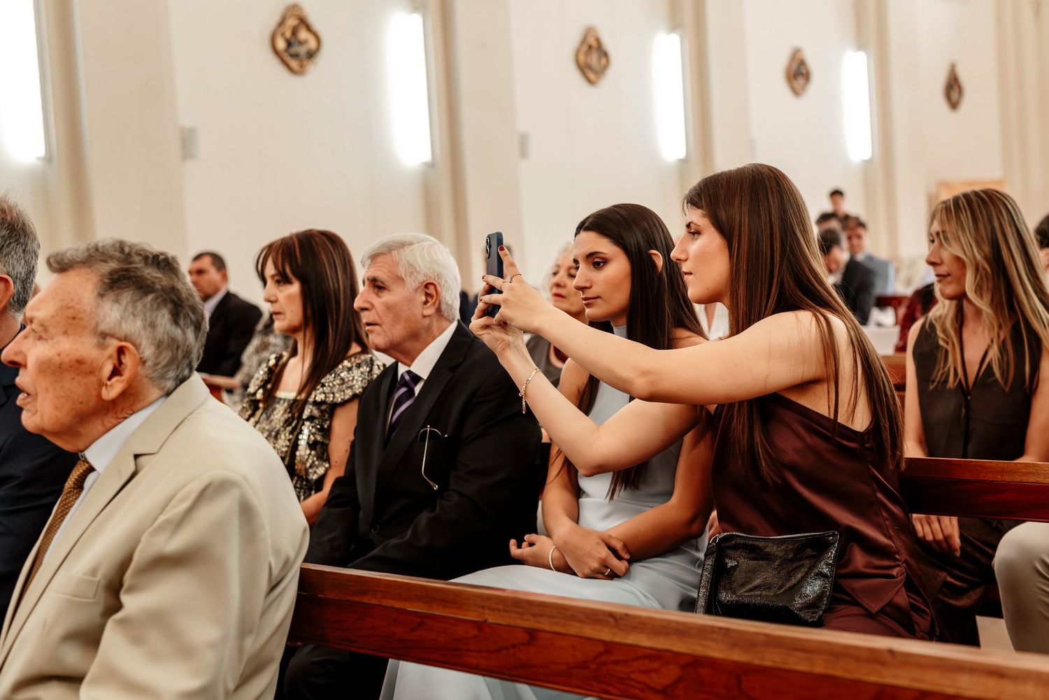 Wedding guests seated in church pews during a ceremony with sunlight streaming through windows.