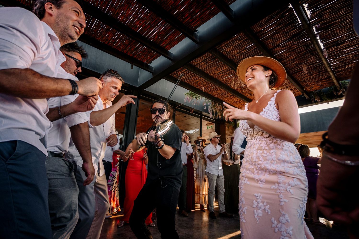 Guests dancing and celebrating at a rustic indoor wedding reception with exposed wooden beams and industrial decor.