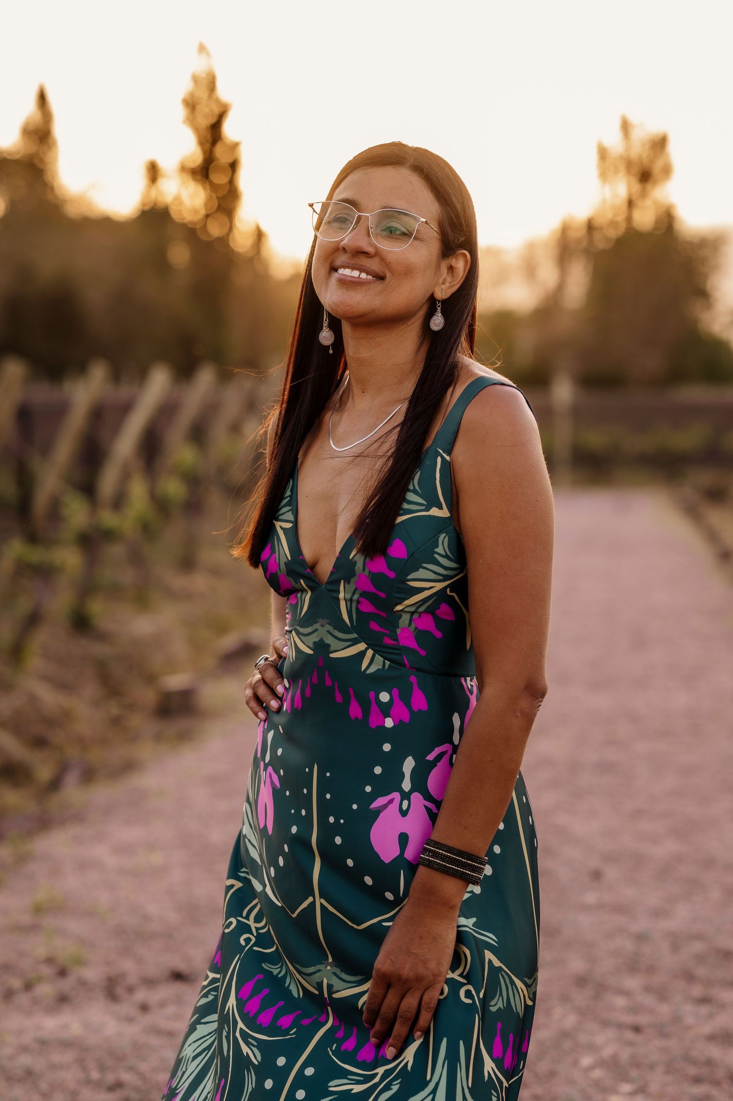 A person in a green floral dress poses outdoors during golden hour sunset in a desert landscape.