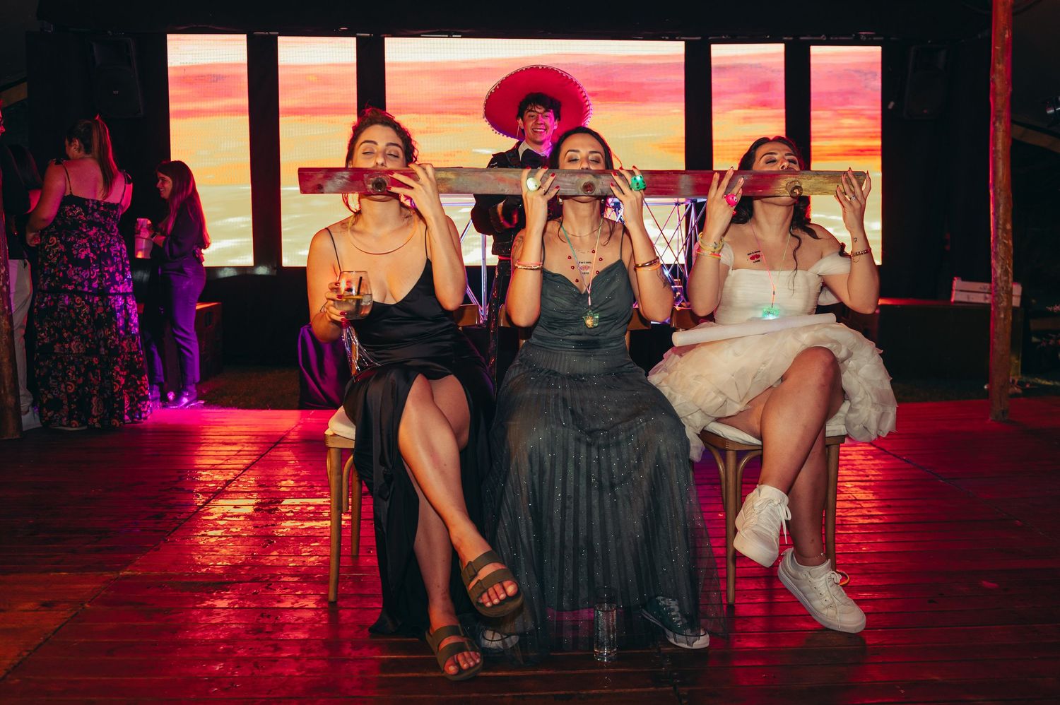 A group of people sitting and socializing in a dimly lit bar or club with red ambient lighting.   fotografos de boda en mendoza