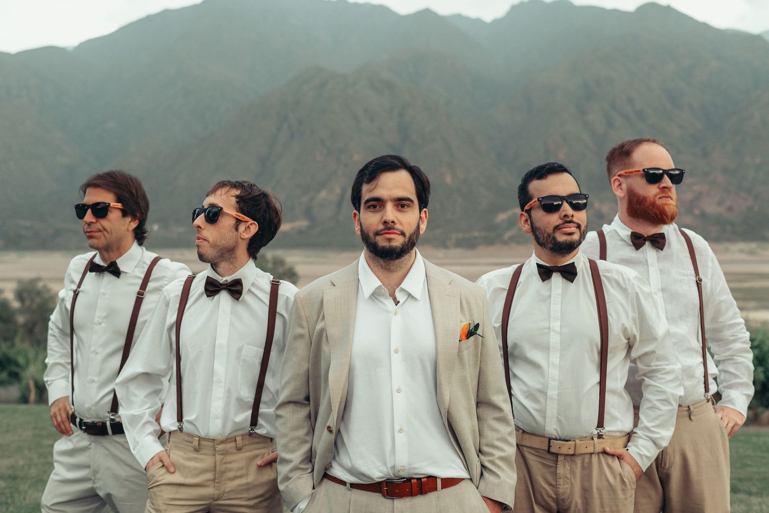 Groomsmen in vintage-inspired attire with suspenders and bow ties pose together against a mountain backdrop.