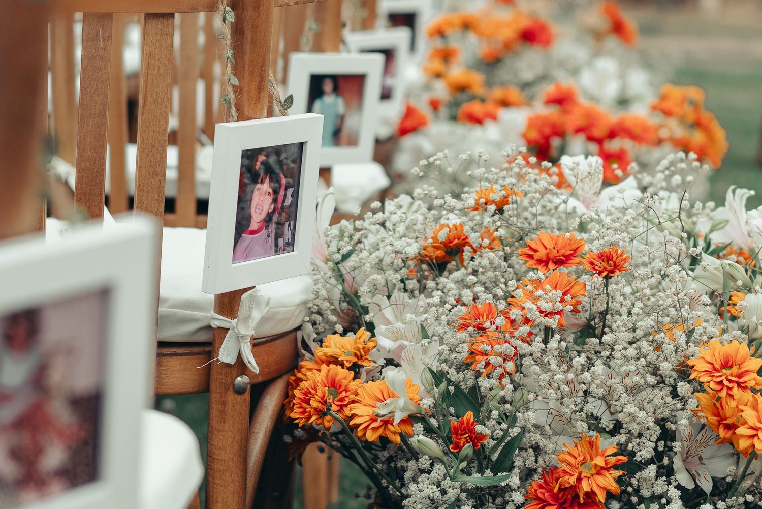 Orange marigolds and white floral arrangements line a wooden railing at an outdoor event.