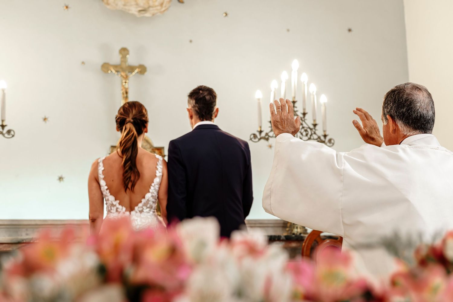 Wedding ceremony attendees stand in a church with hands raised in worship during a religious service.