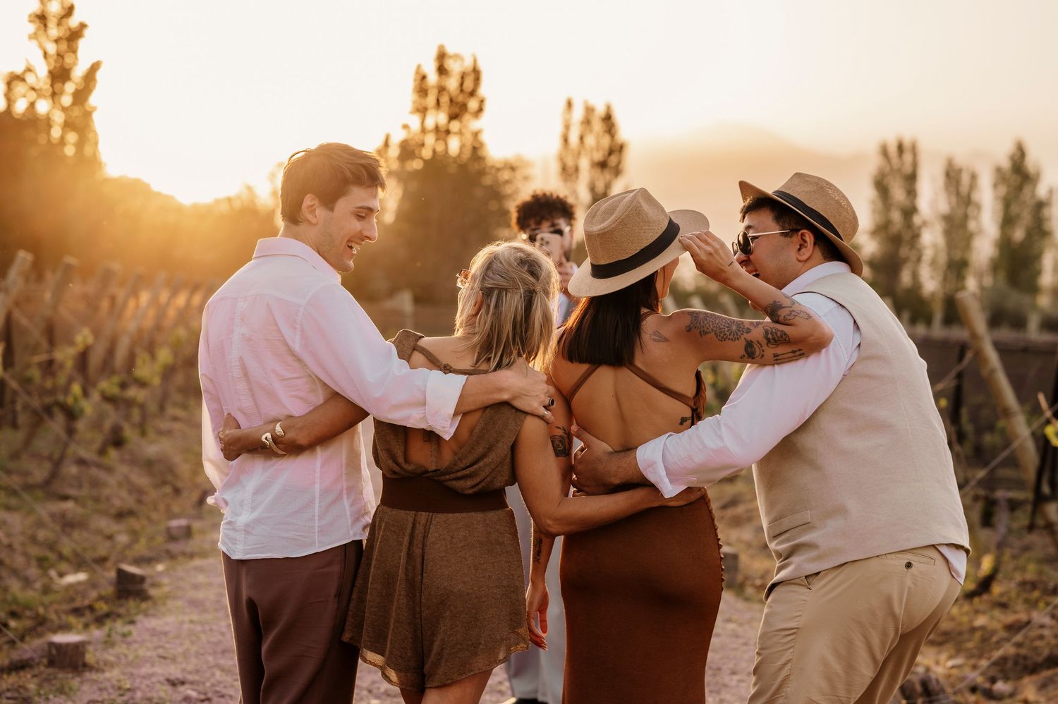 Couple embraces in golden sunset light while dancing in a rustic outdoor setting with trees in background.