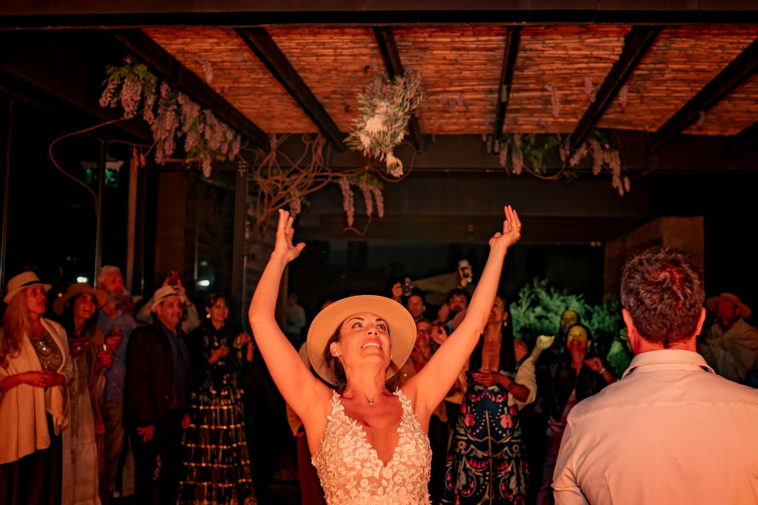 Wedding guests dancing and celebrating on a dance floor with arms raised during a reception party.