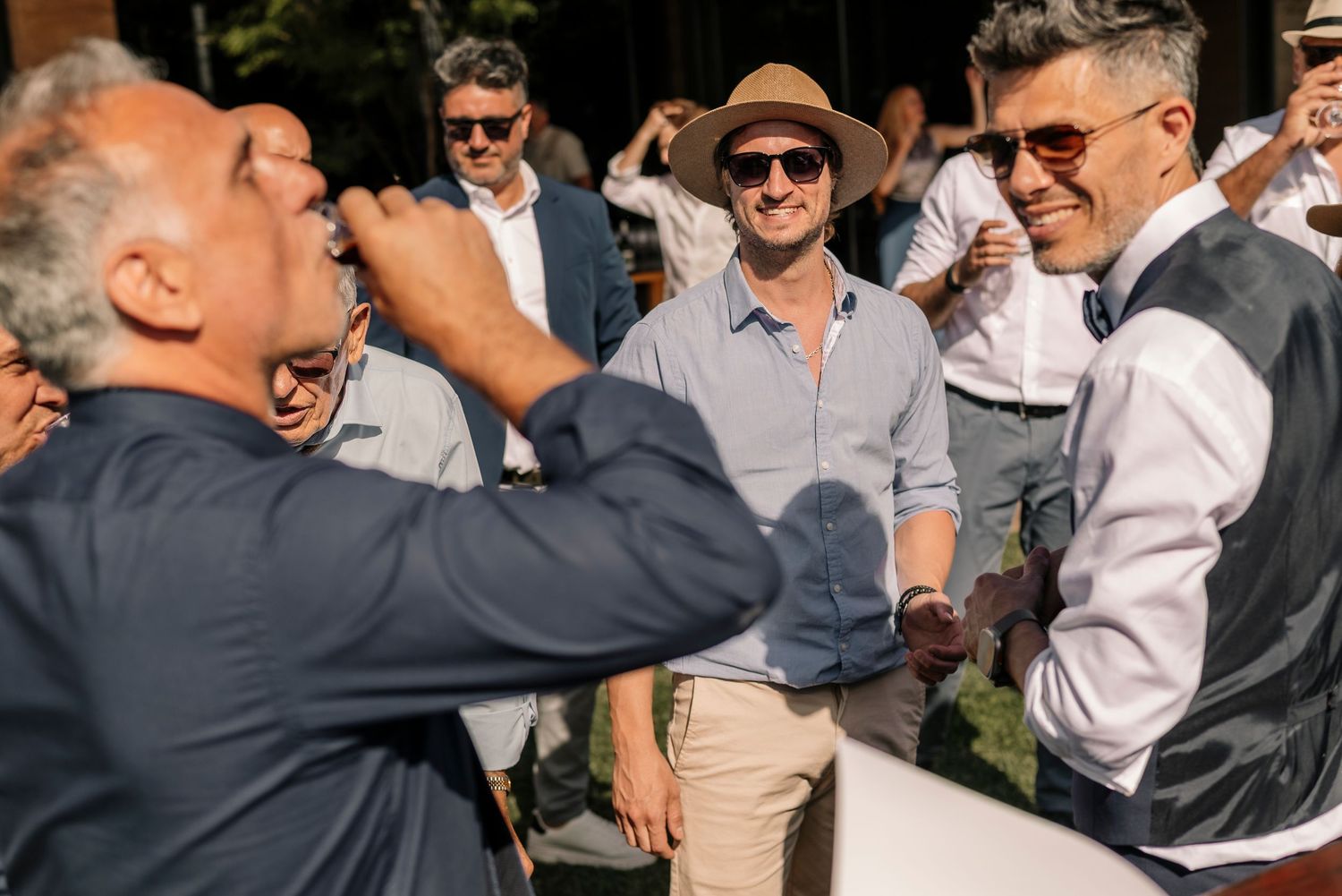 A group of people in formal attire laughing and socializing at an outdoor gathering.